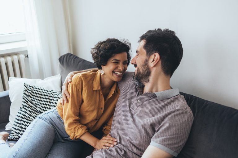 Ein glückliches Paar, das auf dem gemütlichen Sofa sitzt und lacht, während es sich zu Hause entspannt